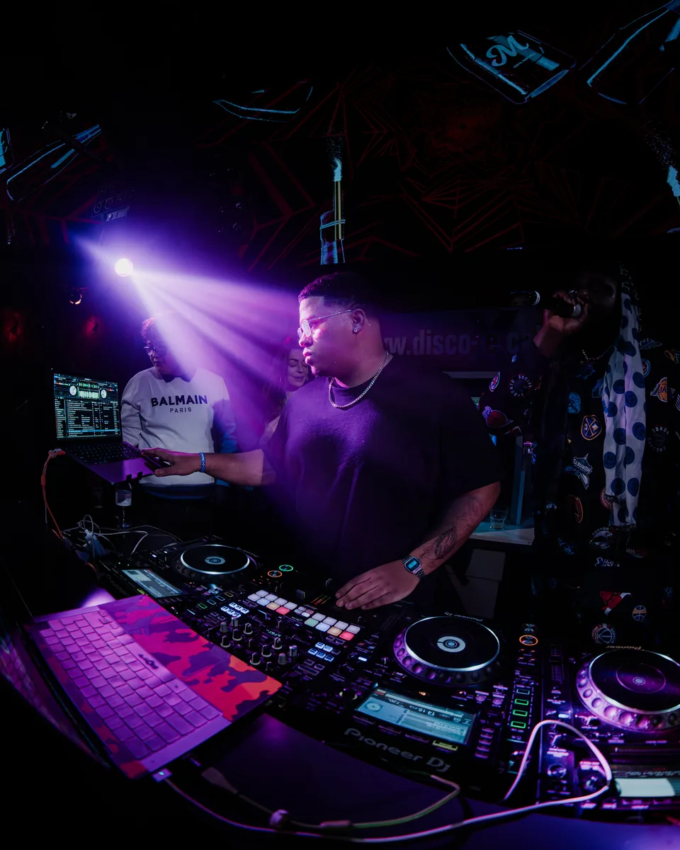 Milkshake – DJ am Mischpult unter violetten Lichtstrahlen