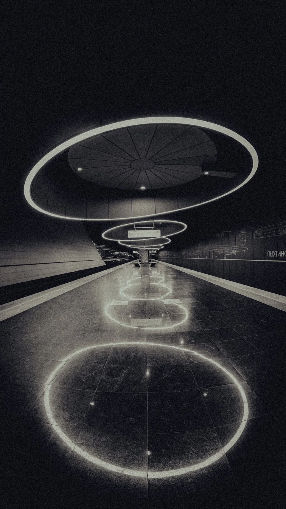 Schwarz-Weiß-Aufnahme einer Metrostation mit ringförmigen Lichtinstallationen